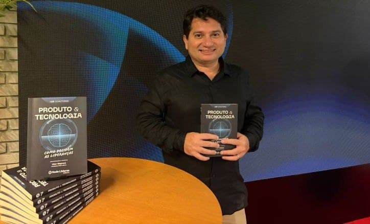 Gustavo Mistrinelli segurando o livro Produto & Tecnologia: Como decidem as lideranças, ao lado de uma pilha de exemplares