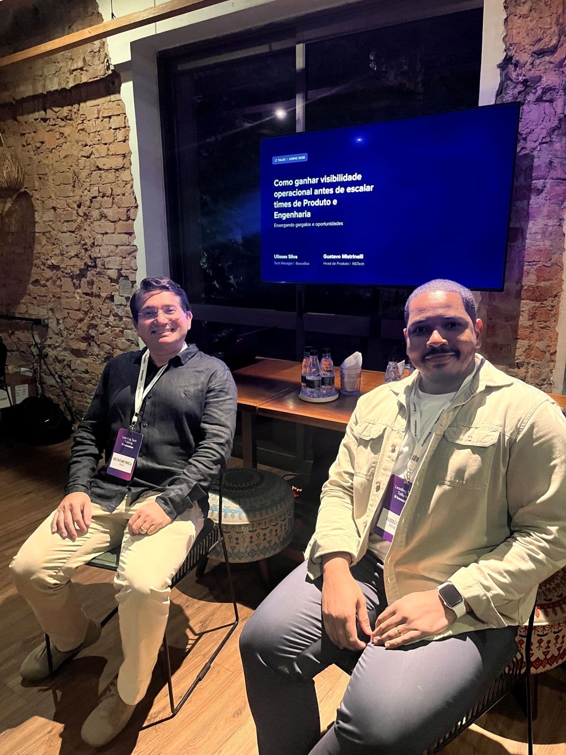 Gustavo Mistrinelli e Ulisses Silva sentados no painel do Leading Tech Talks, com a tela ao fundo: Como ganhar visibilidade operacional antes de escalar times de Produto e Engenharia